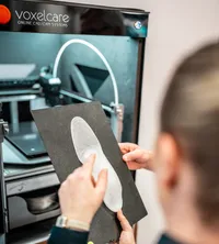 Die Beraterin zeigt auf die frisch-3D-gedruckte Einlage aus dem Voxelcare-3D-Drucker