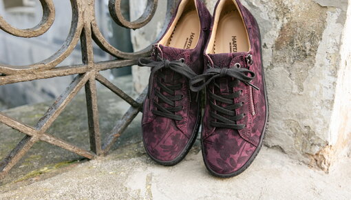 Herbstliche bordeauxfarbene Sneaker mit dezentem Blättermuster stehen an einer Mauer gelehnt.