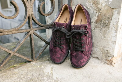 Herbstliche bordeauxfarbene Sneaker mit dezentem Blättermuster stehen an einer Mauer gelehnt.
