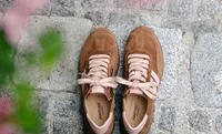Braune Halbschuhe aus Wildleder mit hell rosafarbenen Schnürsenkeln und Details stehen auf Kopfsteinpflaster